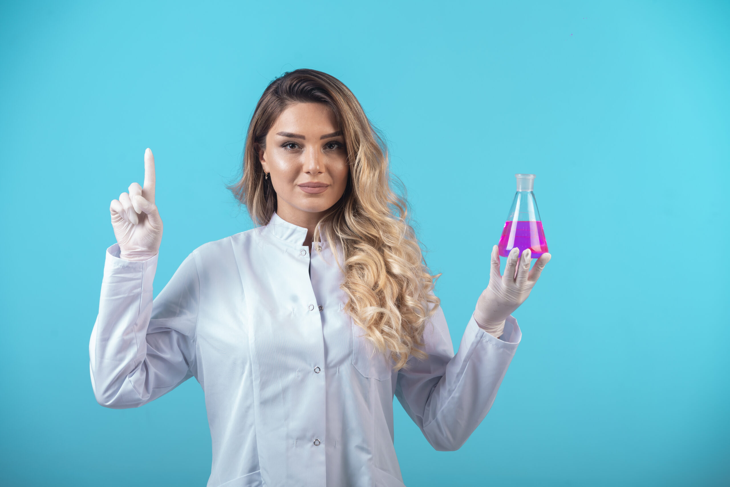 Nurse in white uniform holding a chemical flask with pink liquid and making presentation. High quality photo